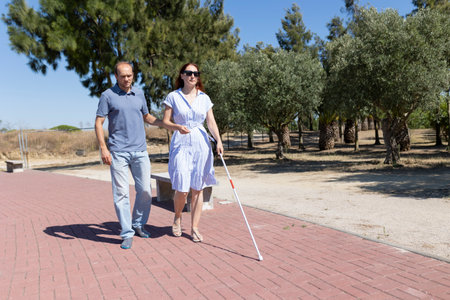Man helping blind woman walking with white cane in park pathの写真素材