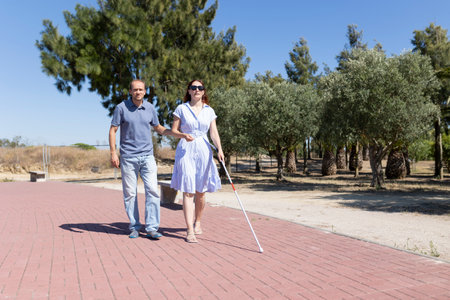 Man helping blind woman walking with white cane in parkの写真素材