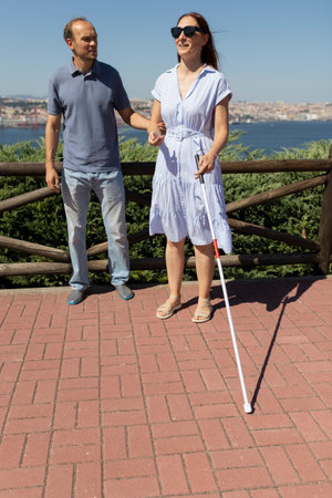 Man helping blind woman with white cane walking in the cityの写真素材