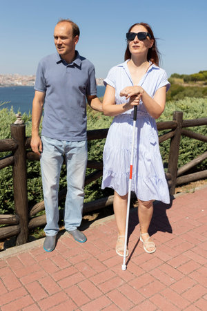 Blind woman holding white cane standing near man in parkの写真素材