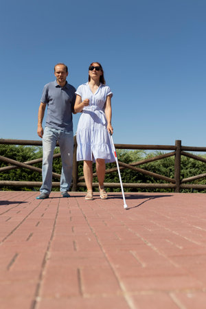 Blind woman walking with white cane and friend in parkの写真素材