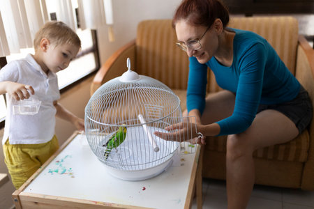 Mother and son caring for pet budgie in cage at homeの写真素材