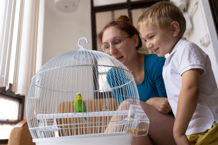 Mother and son admiring a green budgie in its cageの写真素材