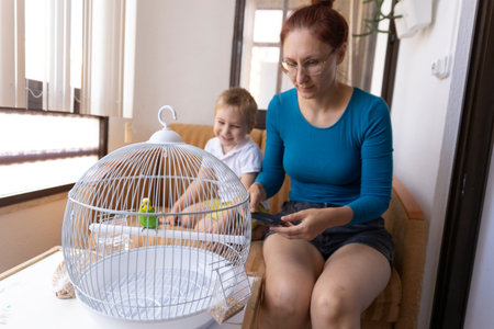 Mother and son admiring a green budgie in a white cage