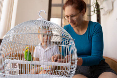 Mother and son observing a parrot in a cage at homeの写真素材