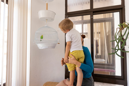 Mother lifting son to see green parrot in hanging cageの写真素材