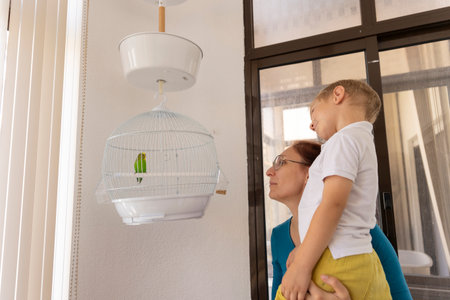 Mother holding her son looking at a green parrot in a cageの写真素材