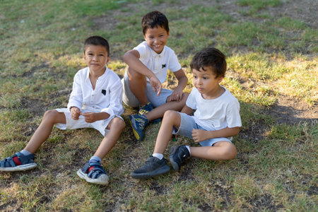 Three children relaxing together on grass in park during summer dayの写真素材