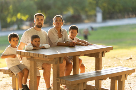 Happy family sitting at picnic table in parkの写真素材
