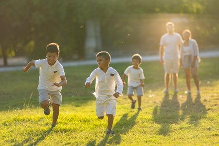 Happy children running in the park with parents watching in the backgroundの写真素材
