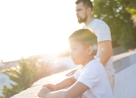 Pensive child leaning on a wall with father at sunsetの写真素材
