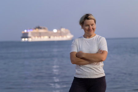 Tourist smiling with arms crossed in front of cruise ship at sunsetの写真素材