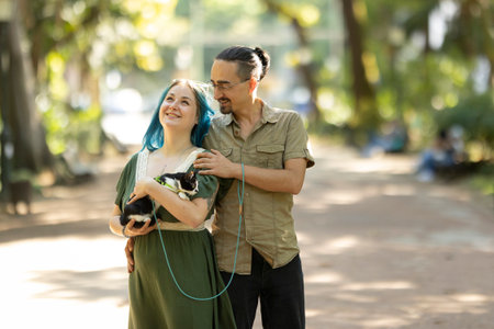 Happy couple walking a cat on a leash in a parkの写真素材