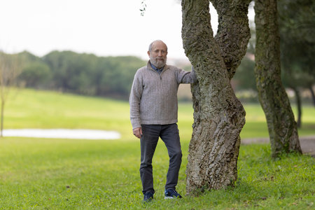 Senior man leaning against a cork oak tree in a green parkの写真素材