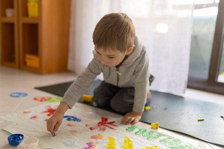 Child painting with fingers on floor at home using colorful tempera colorsの写真素材