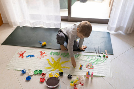 Child painting on floor with tempera colors and brushesの写真素材