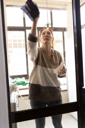 Housewife cleaning windows with rag and detergent spray at home
