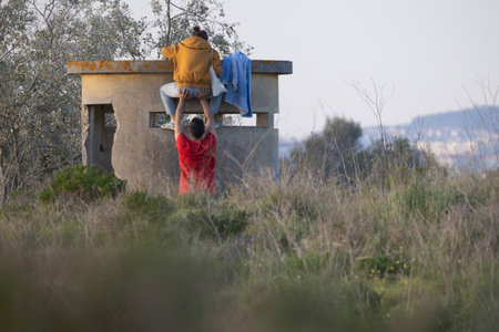 Man lifting woman onto abandoned bunker in tall grass field