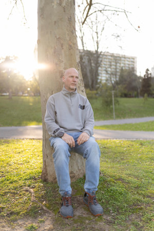 Bald man relaxing under tree in urban park at sunsetの写真素材
