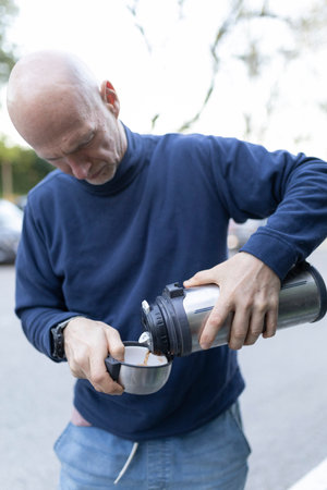 Bald senior man pouring hot drink from thermos into cup outdoorsの写真素材