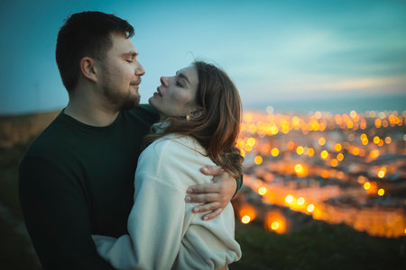 Romantic couple embracing on hilltop overlooking city lights at duskの写真素材
