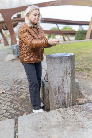 Senior woman washing hands in public park fountainの写真素材