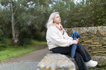 Senior woman relaxing in park holding closed umbrellaの写真素材
