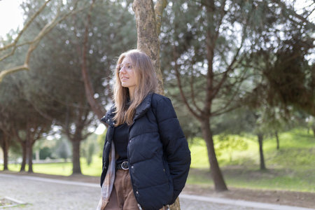 Young woman leaning against tree enjoying park scenery in winter