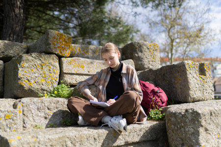 Young woman archaeologist writing notes outdoors on archaeological site