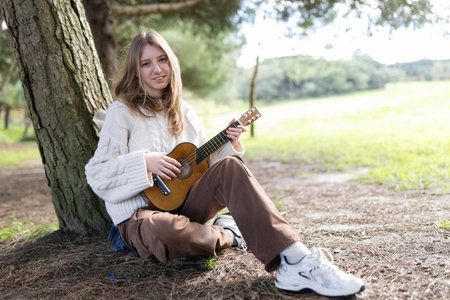 Young woman playing ukulele under tree in nature