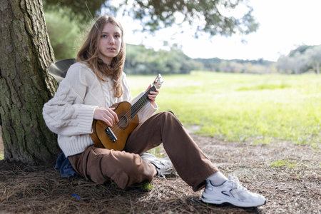 Young musician playing ukulele under a tree in nature
