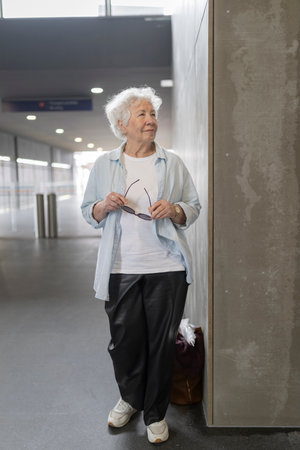 Senior woman waiting in airport terminal holding sunglassesの写真素材
