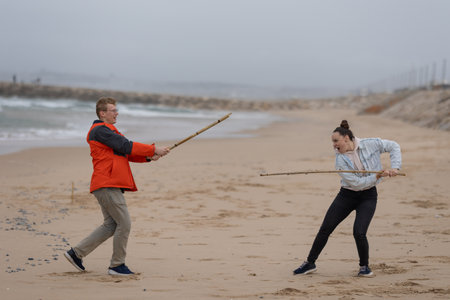 Man and woman playing stick fight battle on beach