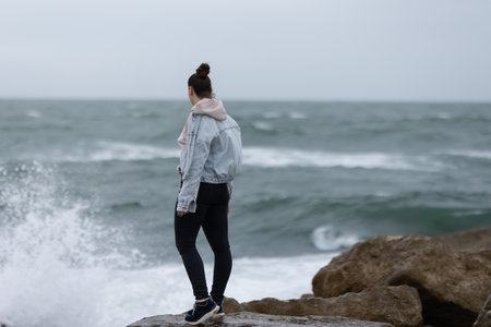 Young woman looking out at powerful ocean wavesの写真素材