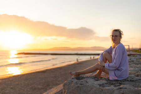 Young woman enjoying tranquil golden hour on beach at sunsetの写真素材