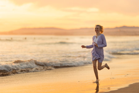 Happy young woman joyfully running on summer beach at sunsetの写真素材