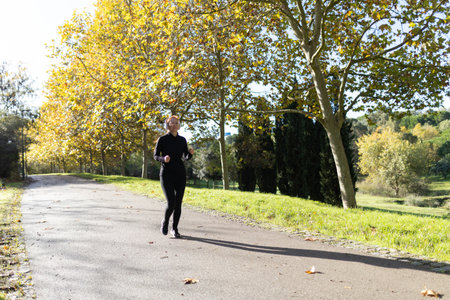 Woman running in autumn park path listening music