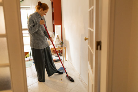 Woman using a broom to clean the floor inside her homeの写真素材