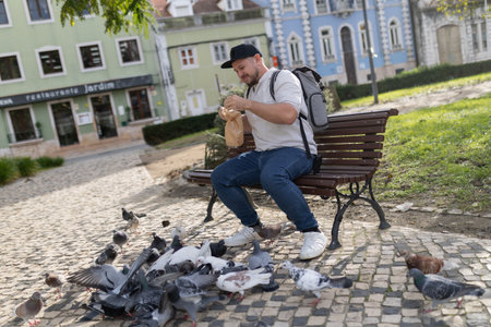 Man feeding pigeons in urban park with street foodの写真素材