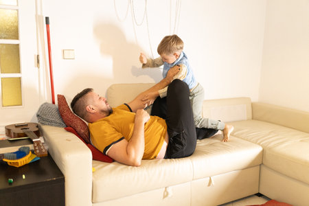 Father and son playing cheerfully on living room couchの写真素材