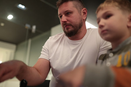Father guiding son while learning or playing indoors