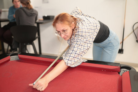 Woman playing billiards aiming cue stick concentrating on game