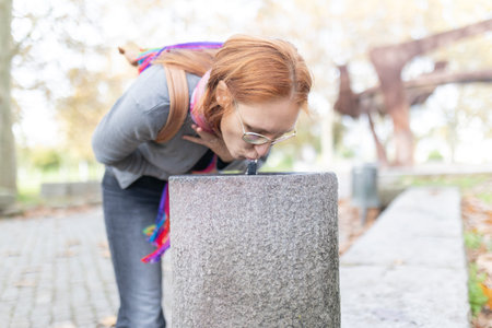 Woman drinking fresh water from public fountain outdoorsの写真素材