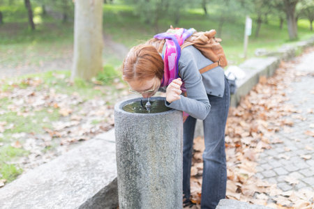 Woman drinking fresh water from public park fountainの写真素材
