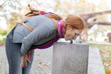 Woman bending down drinking from public water fountainの写真素材