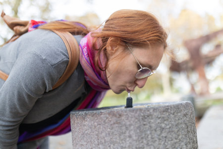 Woman refreshing drinking water from public fountainの写真素材