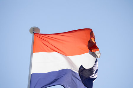 Netherlands flag waving in wind against blue skyの写真素材