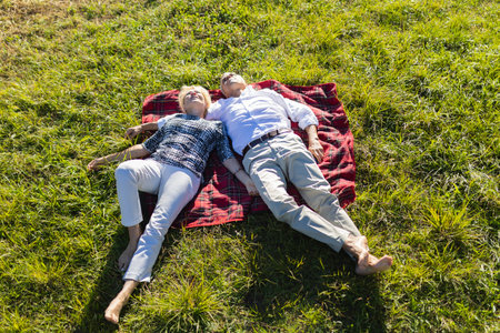 Senior couple relaxing on grass in sunny parkの写真素材