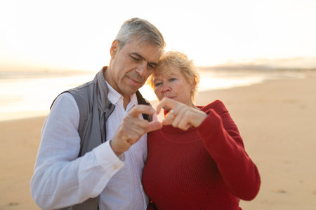 Senior couple sharing love making hand heart on beach