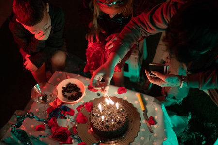 People lighting birthday cake candles during night celebrationの写真素材
